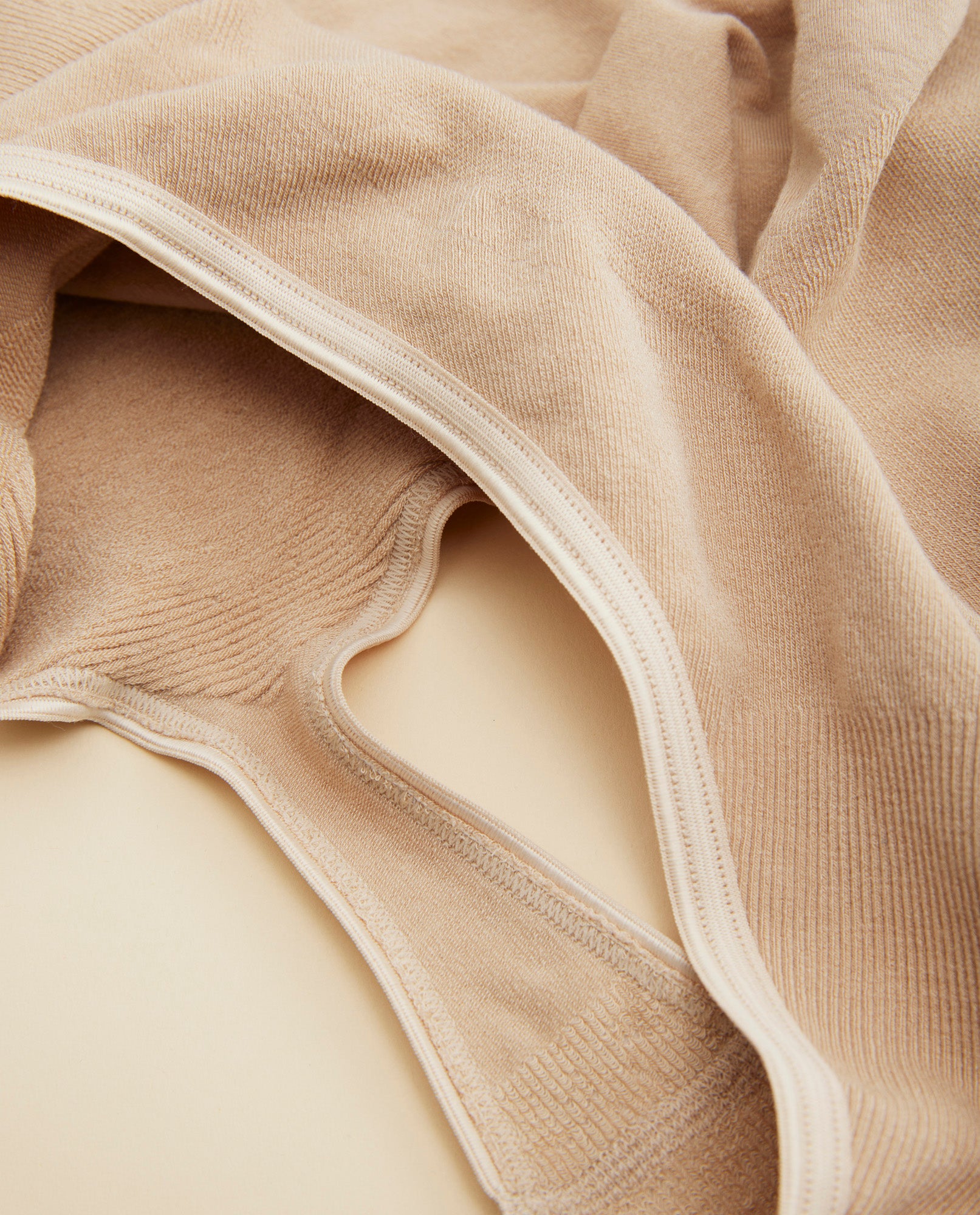 Belly support g-streng i farven sand, der ligger ned, så man kan se detaljerne omkring syninger i stoffet.