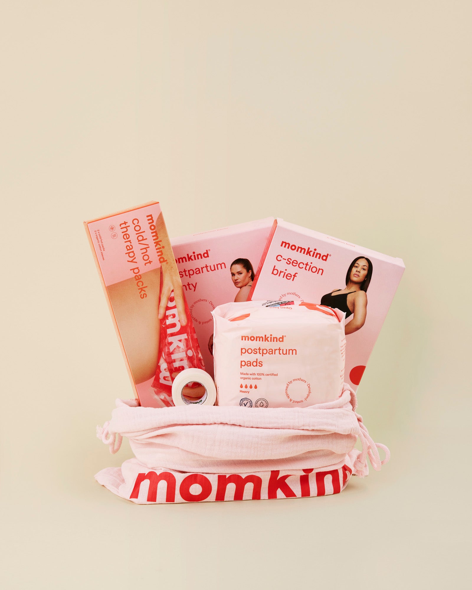 Momkind mellem efterfødselspakke til kejsersnit. Posen indeholder englehud plaster, efterfødselsbind, efterfødselstrusser, kejsersnittrusser og køle/varme pose.
