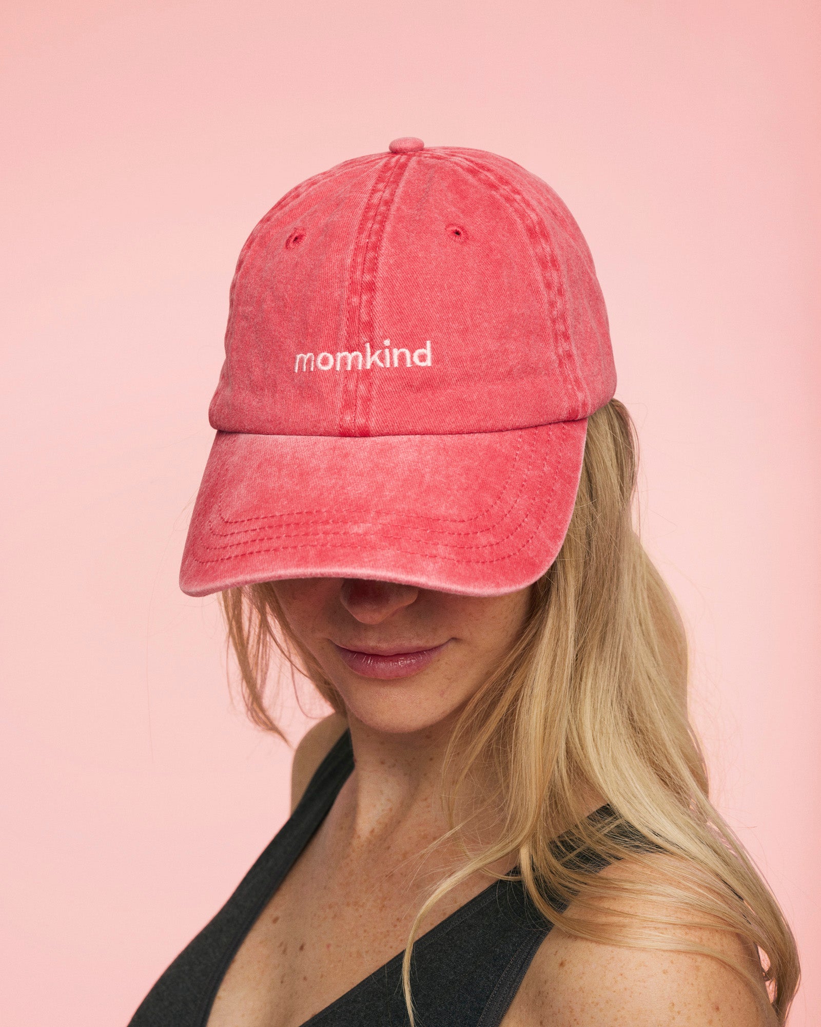 Momkind cap I rød med lyserød logo. Den sidder på kvindes hovede som kigger ned.