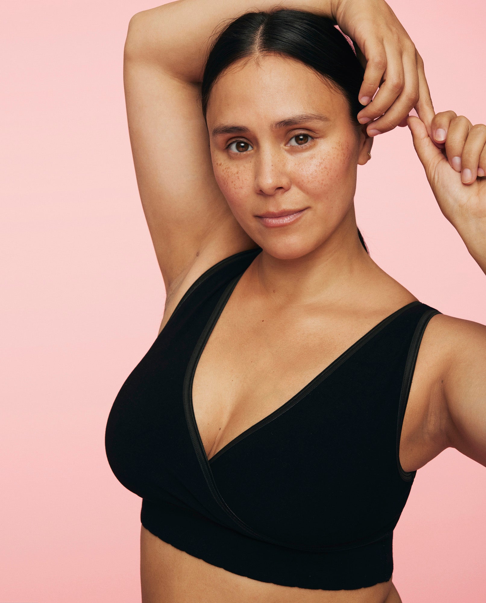 kvinde står med den ene arm over hovedet iført crossover bh i sort fra momkind
