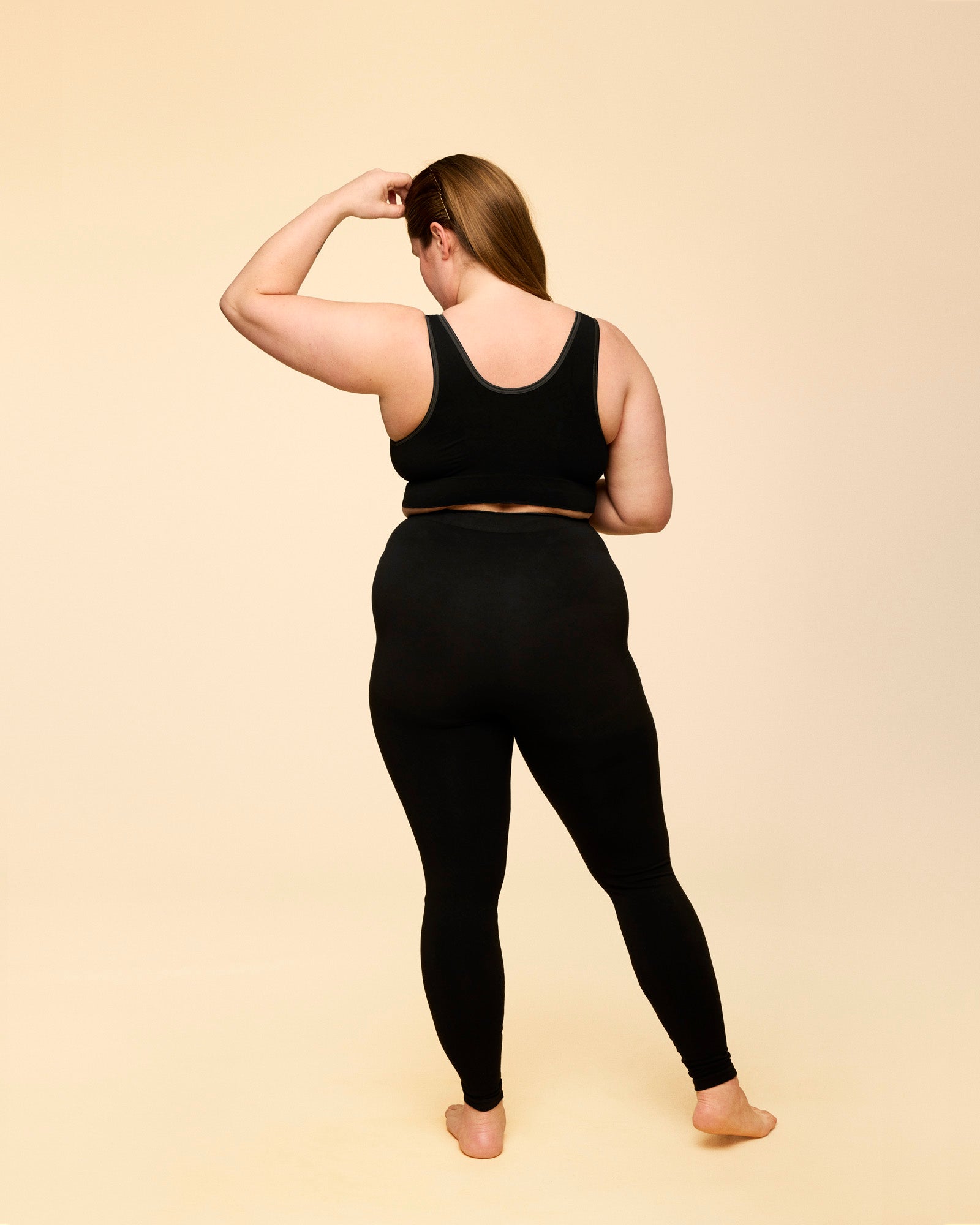 Plus size model står med ryggen til iført momkind hugwear efterfødselsleggings i sort. De går op over lænden og er højtaljede på modellen.