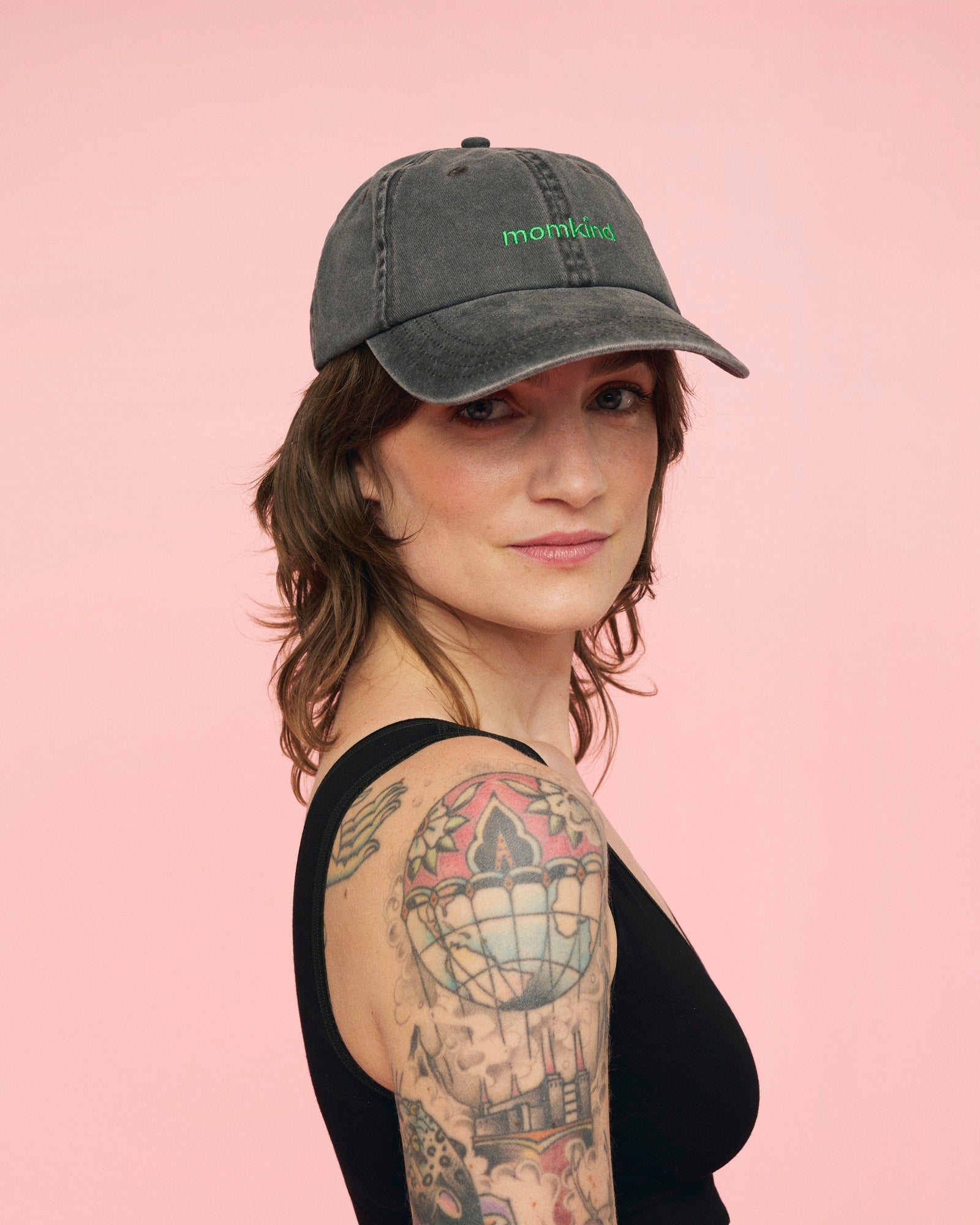 Momkind cap I sort med grønt logo. Den sidder på hovedet af en kvinde, hvor den kan ses forfra.