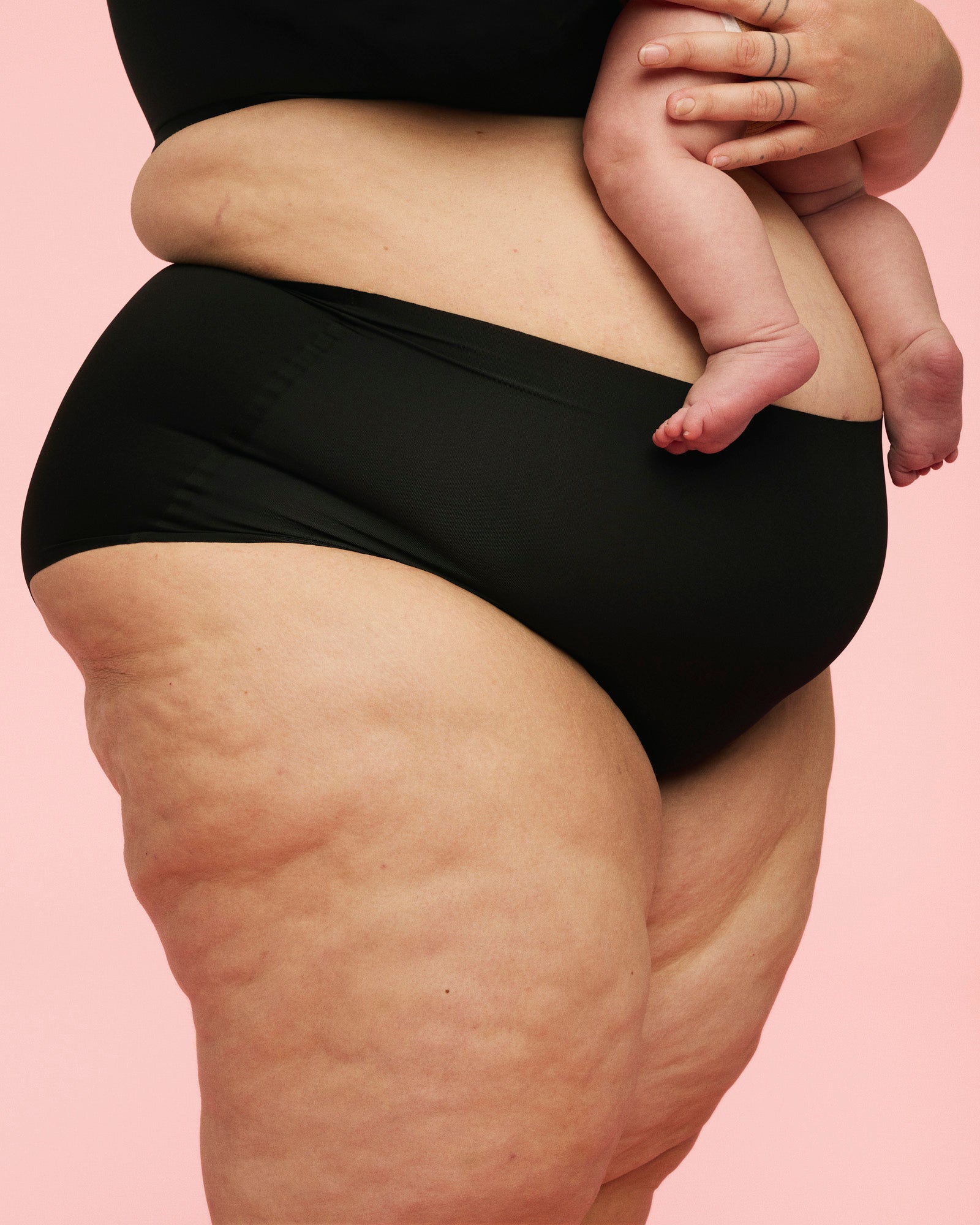 Plus size kvinde iført højtaljede sømløse trusser fra momkind i sort, mens hun bærer barn.