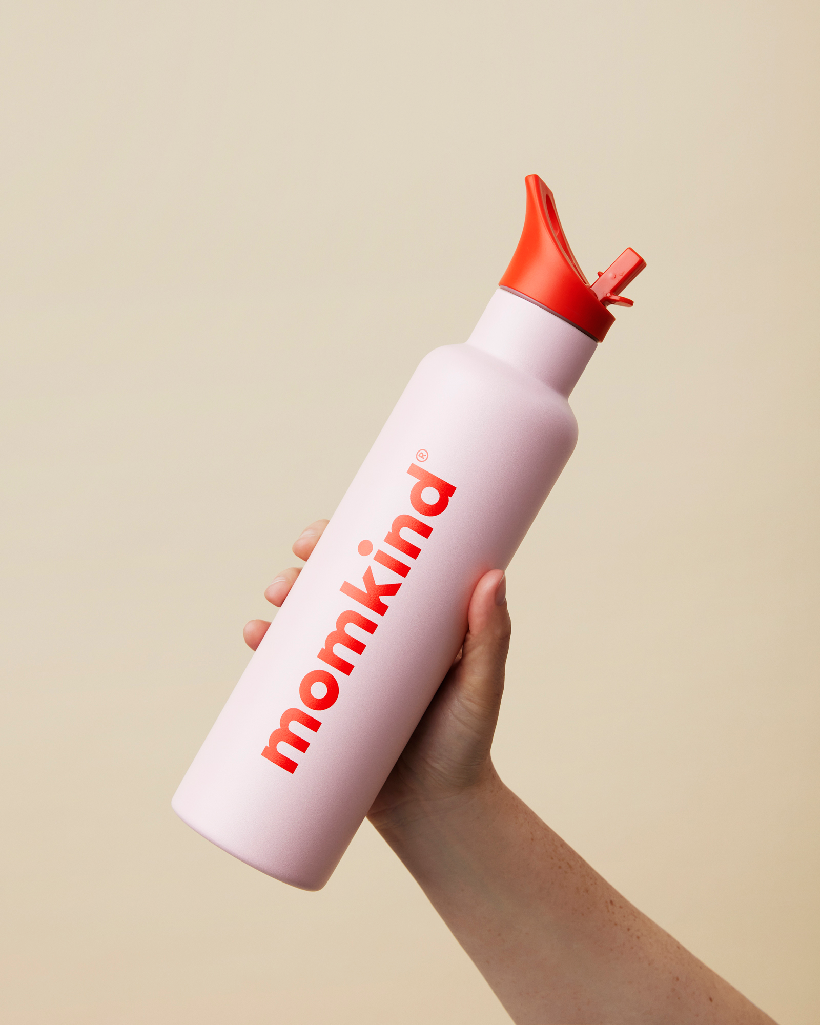 hånd holder lyserød termo drikkedunk med sugerør og rødt låg fra momkind