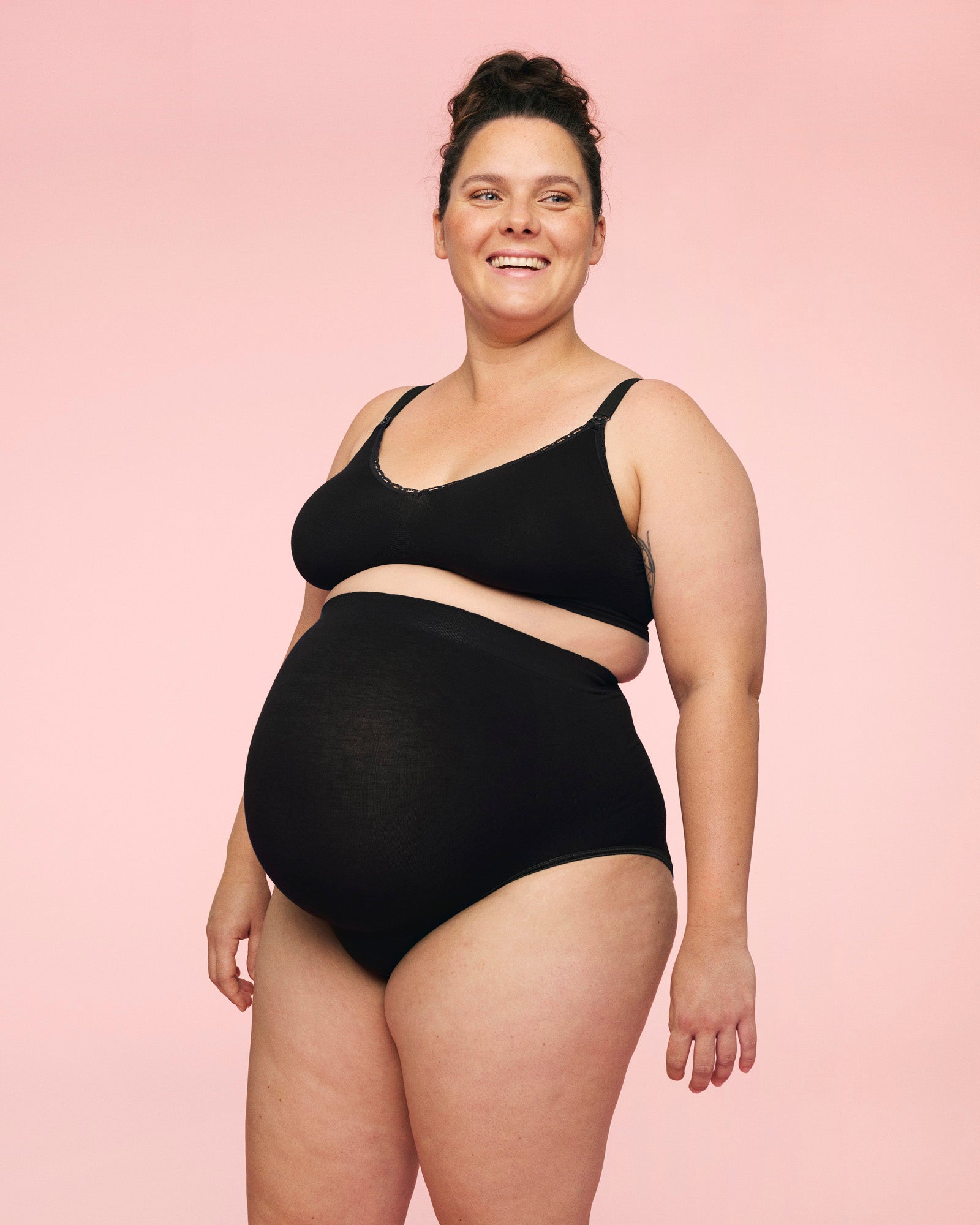 Smilende gravid kvinde iført momkind graviditetstrusse med matchende amme bh i sort. 