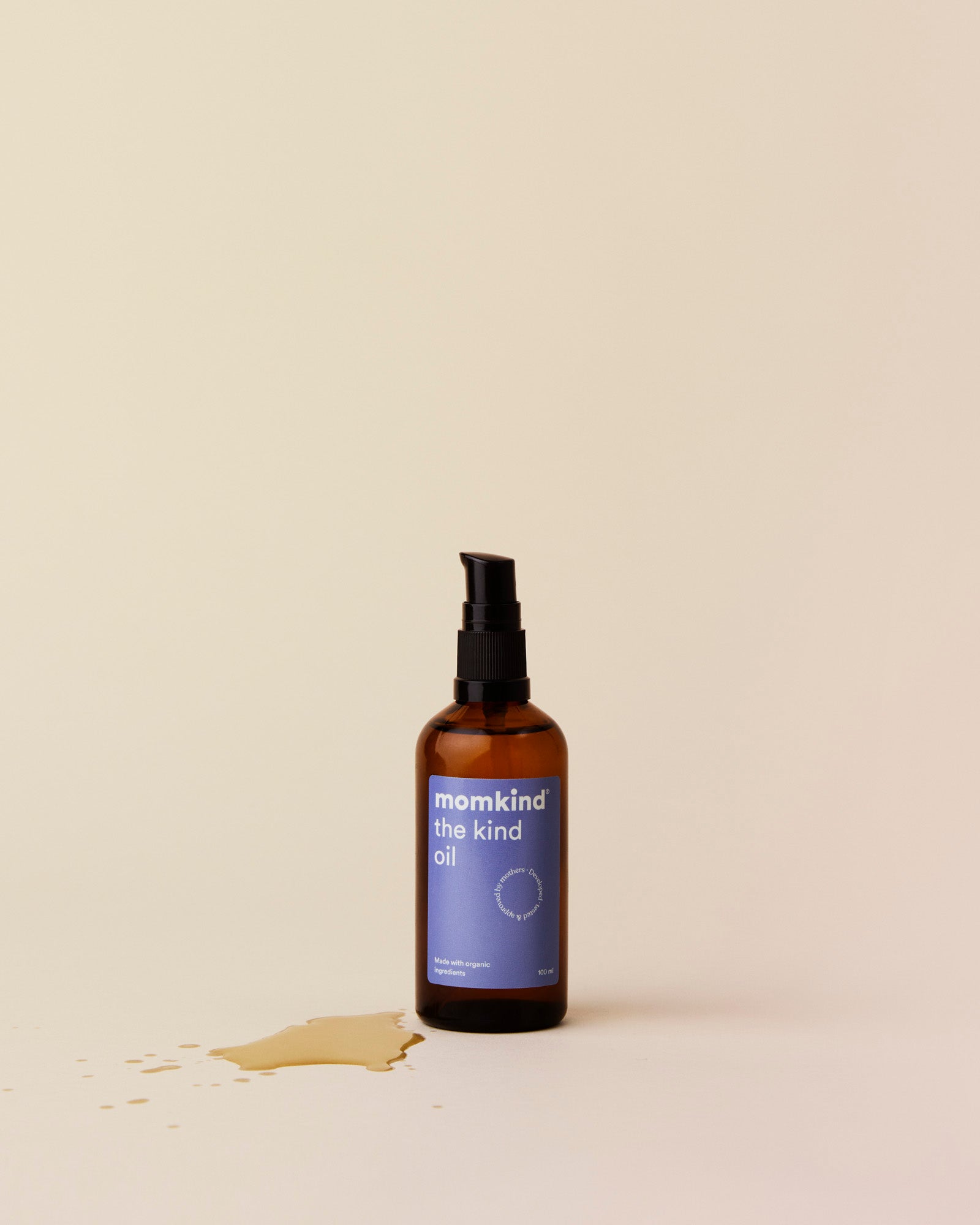 Brun glasflakse med sort pumpe, med teksten momkind the kind oil. Der er spildt lidt olie foran flasken.